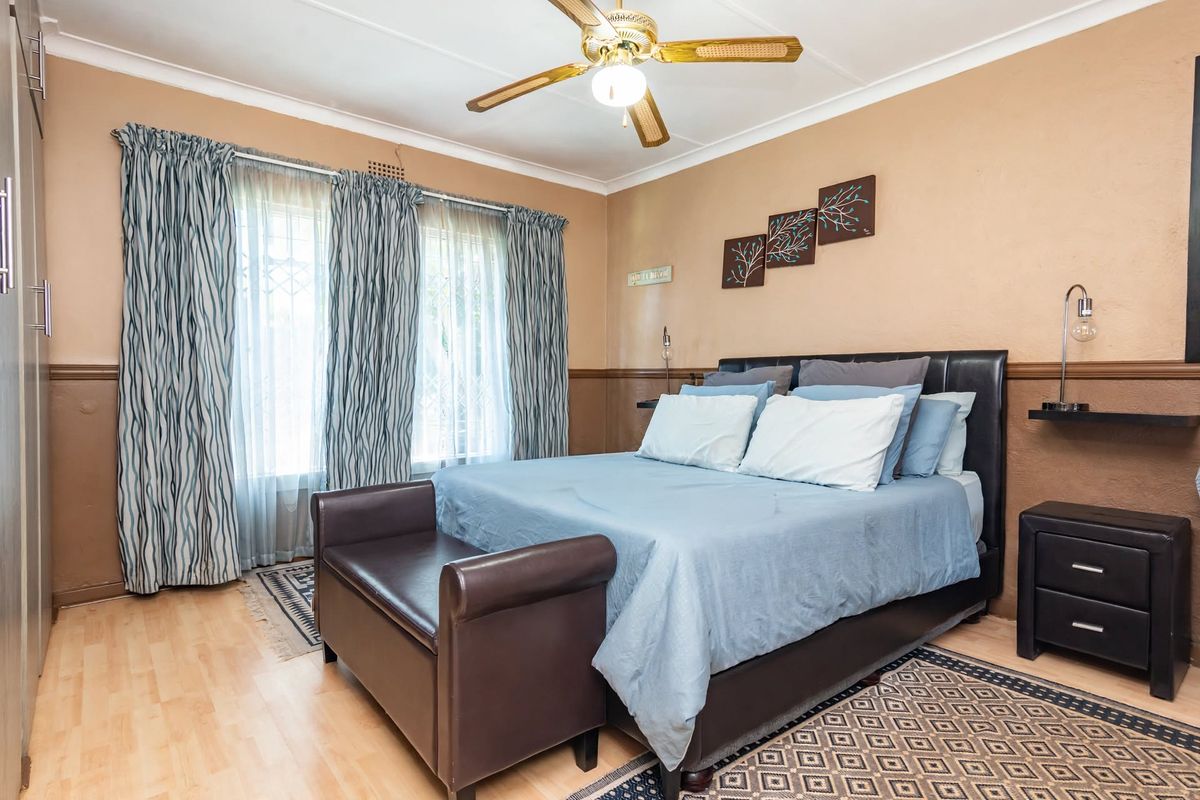 A well-maintained bedroom featuring laminate flooring, built-in cupboards, and a ceiling fan, offering a comfortable and functional living space.