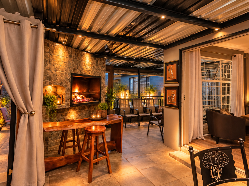 A well-appointed covered patio featuring a built-in braai with stone cladding, tiled flooring, and recessed lighting, seamlessly connecting to the indoor living area.