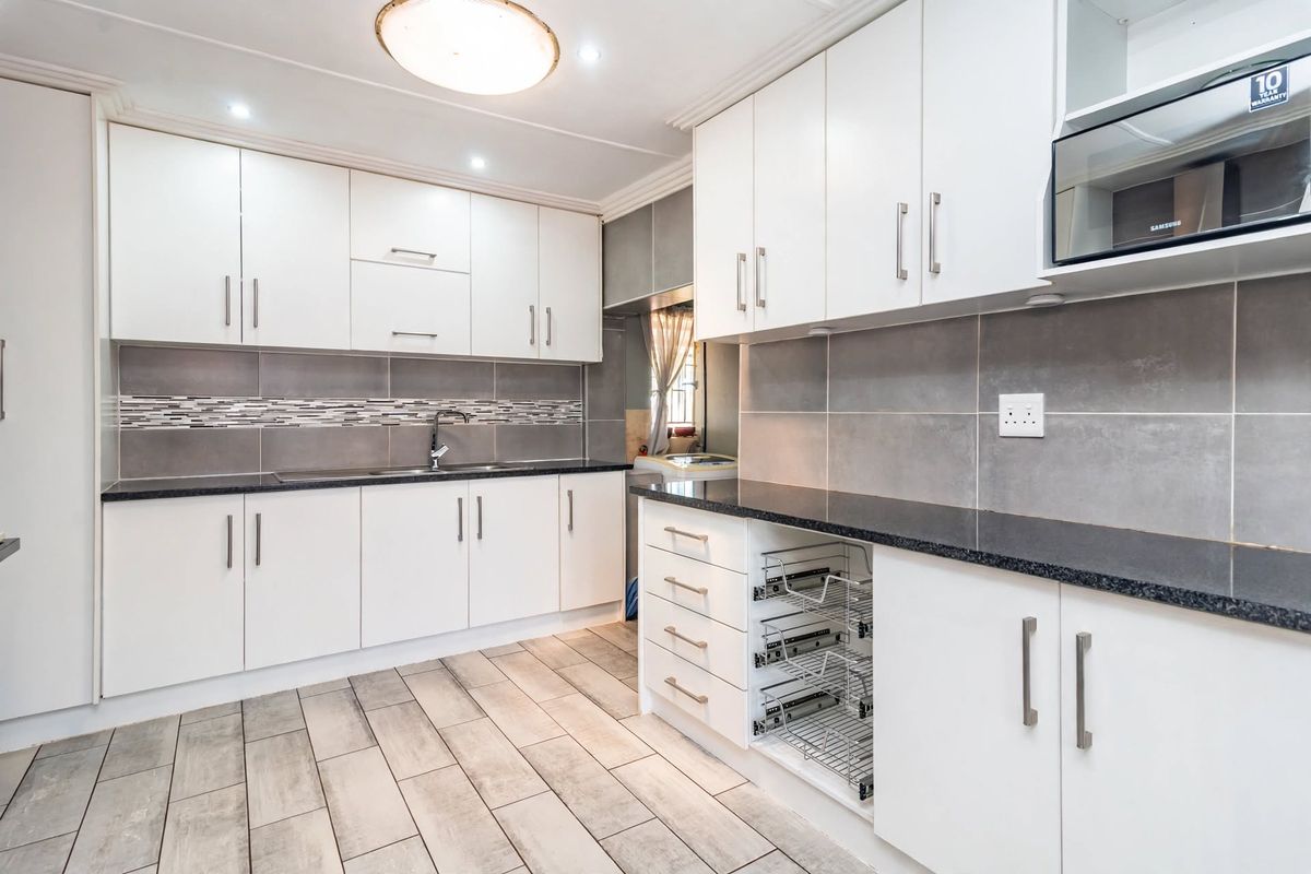 Modern kitchen featuring white cabinetry, dark granite countertops, grey tiled backsplash, and integrated microwave with convenient pull-out storage drawers.