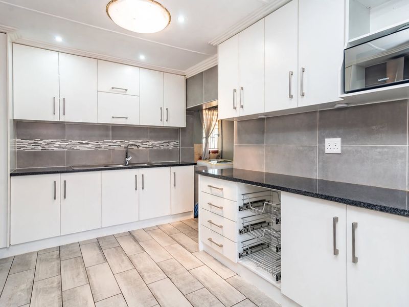 Modern kitchen featuring white cabinetry, dark granite countertops, grey tiled backsplash, and integrated microwave with convenient pull-out storage drawers.