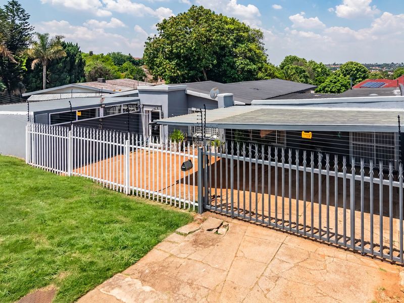 Front exterior view of the property featuring a paved driveway, carport, and secure boundary wall with electric fencing.