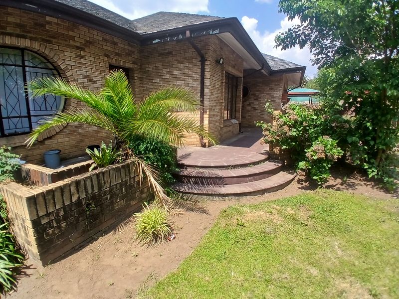 Rear exterior view of a brick house featuring a curved staircase, arched window, and established garden area.
