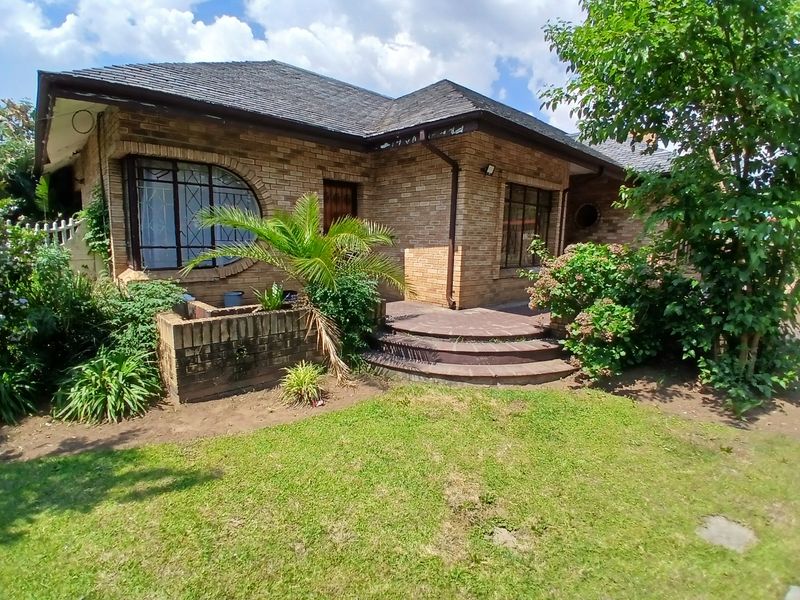 Front elevation of a brick house featuring a curved window, tiled roof, and paved entrance steps set within a landscaped garden.