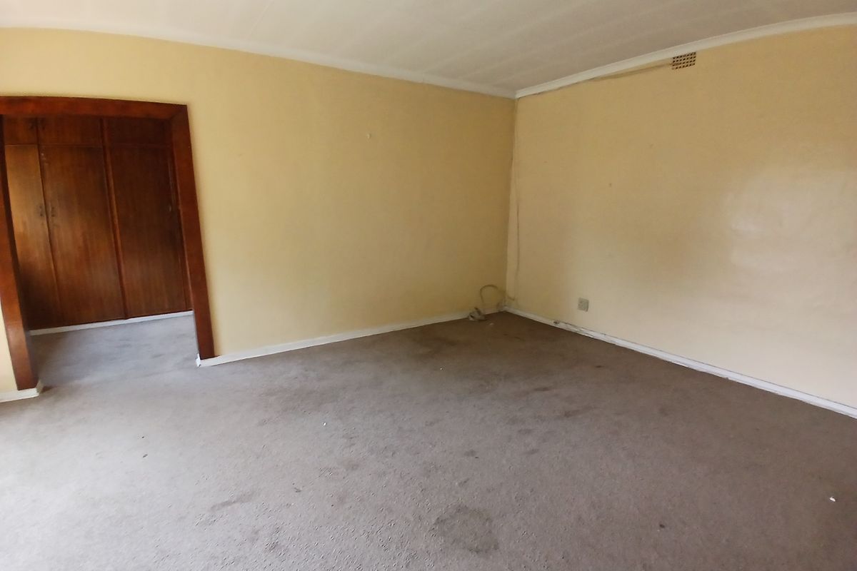 An empty bedroom featuring built-in wooden cupboards, a ceiling fan, and carpeted flooring in need of replacement.