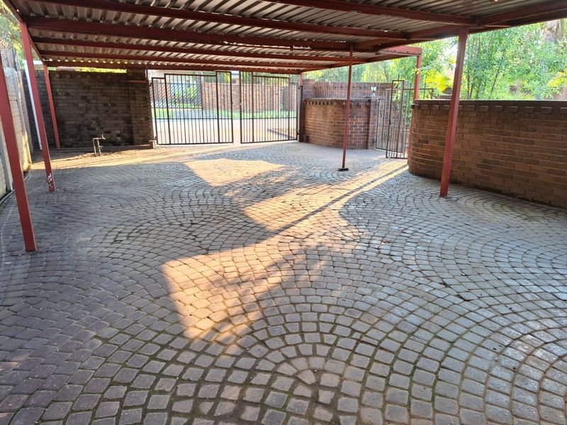 A spacious covered carport featuring durable cobblestone paving, secure metal gates, and sturdy brick boundary walls, providing ample off-street parking space.