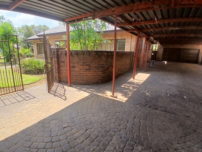 A spacious covered carport area featuring paved flooring, a brick boundary wall, and metal structural supports, providing ample parking space.