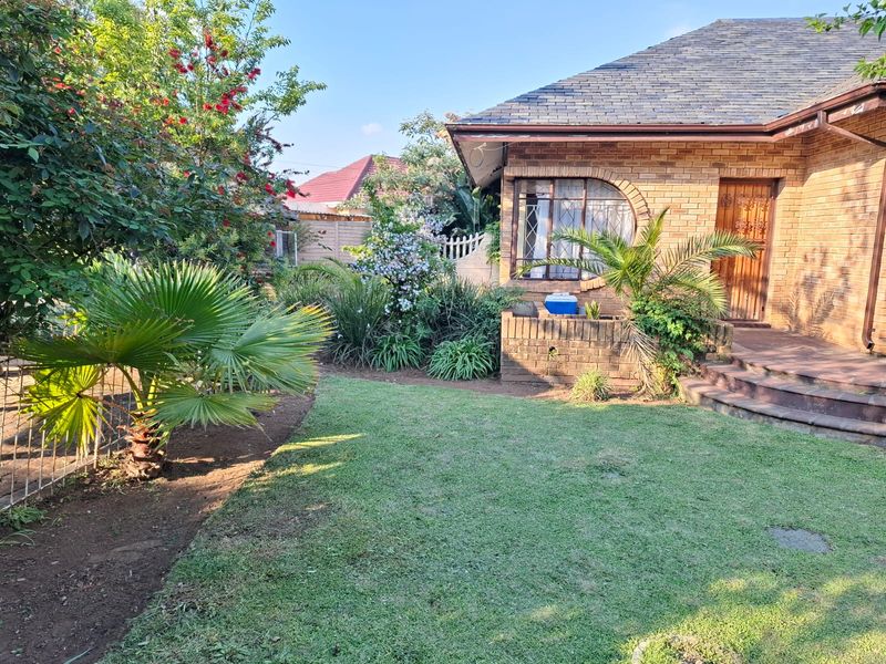 A well-maintained face brick home featuring an arched window, secure entrance, and a landscaped front garden with established greenery.