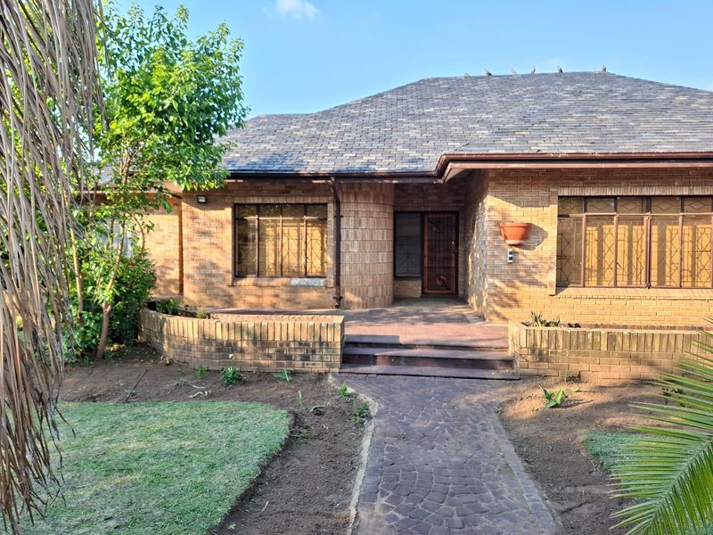 Front elevation of a single-story brick house featuring a tiled roof, paved entrance walkway, and established garden area.