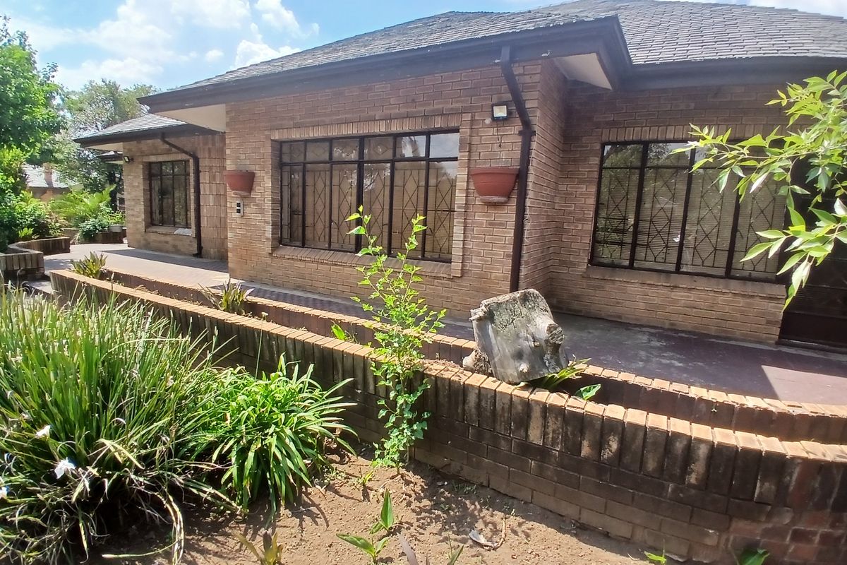 A rear view of a face brick house featuring a paved patio area and a low brick retaining wall in the garden.