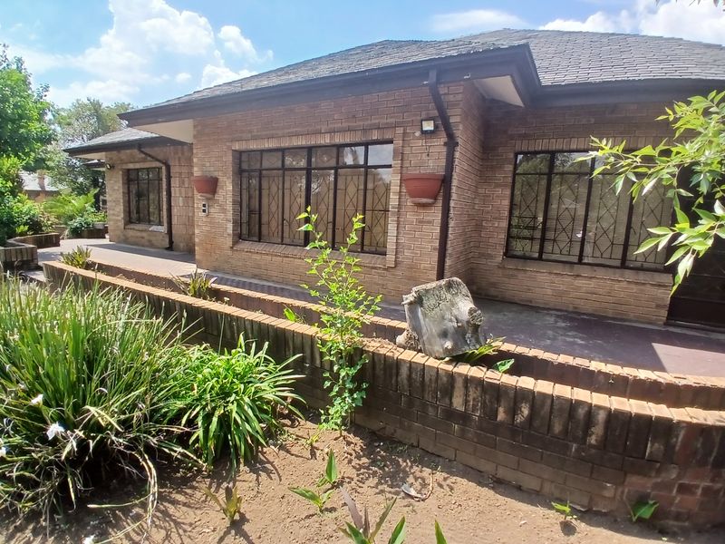 A rear view of a face brick house featuring a paved patio area and a low brick retaining wall in the garden.