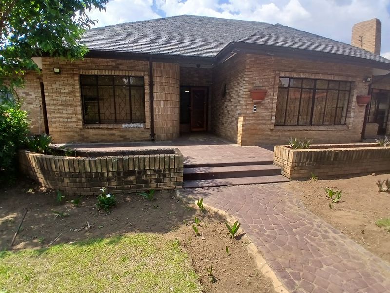 Front elevation of a face brick house featuring a hipped roof, paved entrance walkway, and established brick retaining walls in the front garden.