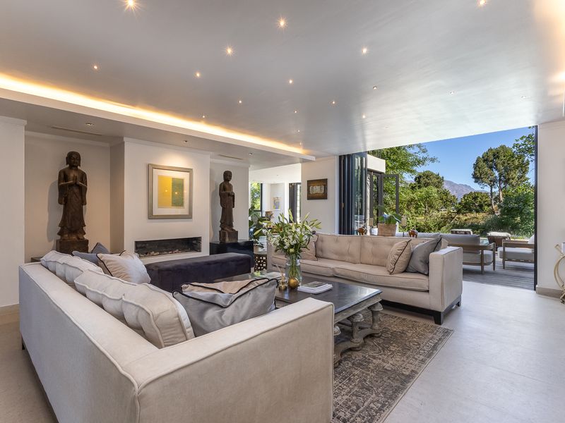 Spacious open-plan living area featuring recessed and cove lighting, a built-in fireplace, and large sliding doors opening to an outdoor patio.