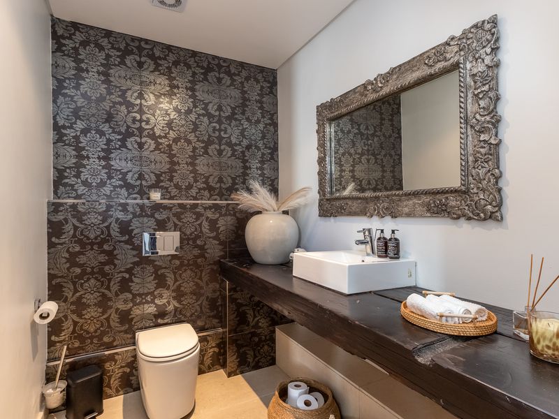 A stylish guest bathroom featuring a floating timber vanity, vessel sink, wall-mounted toilet with concealed cistern, and decorative feature wall tiling.