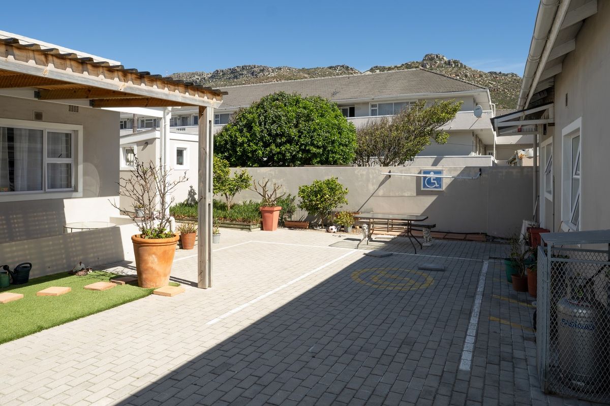 A paved rear courtyard area featuring a timber pergola, designated parking space, and boundary wall with mountain views.