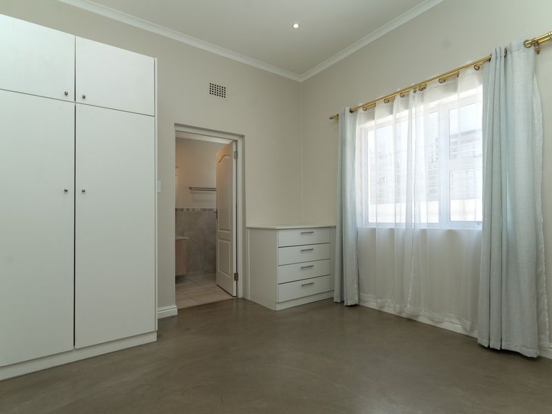 A bright, neutral bedroom featuring polished concrete floors, built-in cabinetry, and an en-suite bathroom entrance, offering a clean and modern blank canvas.