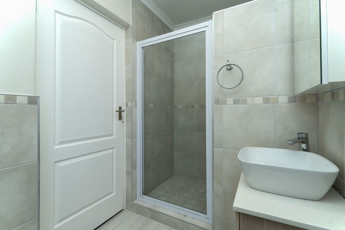 A clean, modern bathroom featuring a glass-enclosed shower, a contemporary vessel sink on a vanity cabinet, and neutral wall and floor tiling.