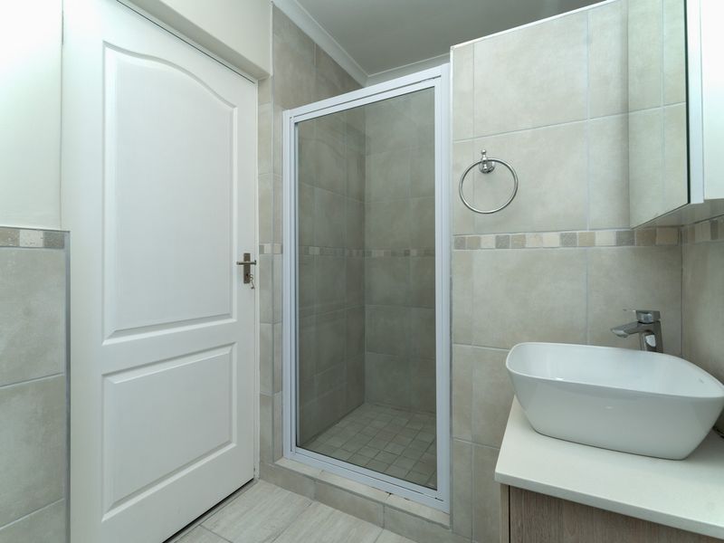 A clean, modern bathroom featuring a glass-enclosed shower, a contemporary vessel sink on a vanity cabinet, and neutral wall and floor tiling.