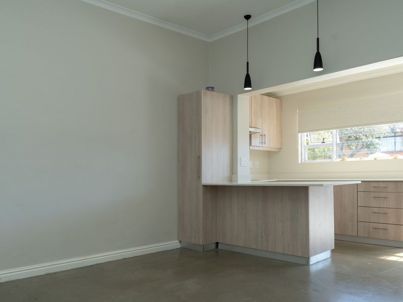 An open-plan kitchen area featuring light-wood cabinetry, stone-look countertops, polished concrete floors, and modern pendant lighting in a clean, vacant space.