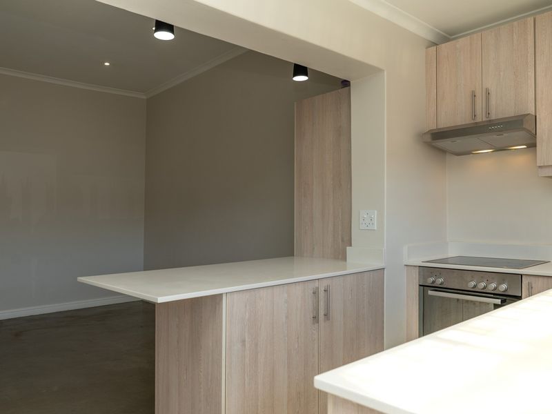 Modern open-plan kitchen featuring light wood-grain cabinetry, stone countertops, integrated oven and hob, and a functional breakfast bar area.