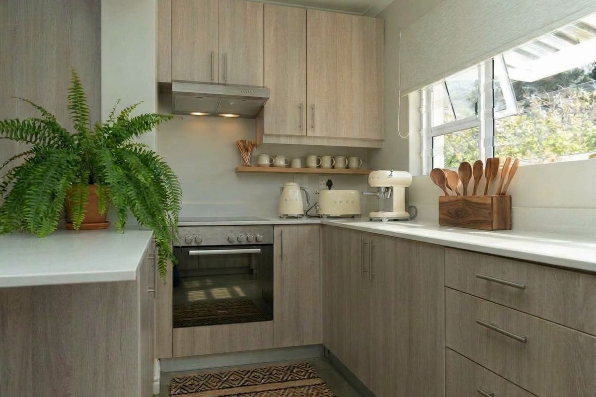 A modern, well-maintained kitchen featuring light wood-grain cabinetry, integrated oven and hob, extractor fan, and clean stone countertops with ample natural light.