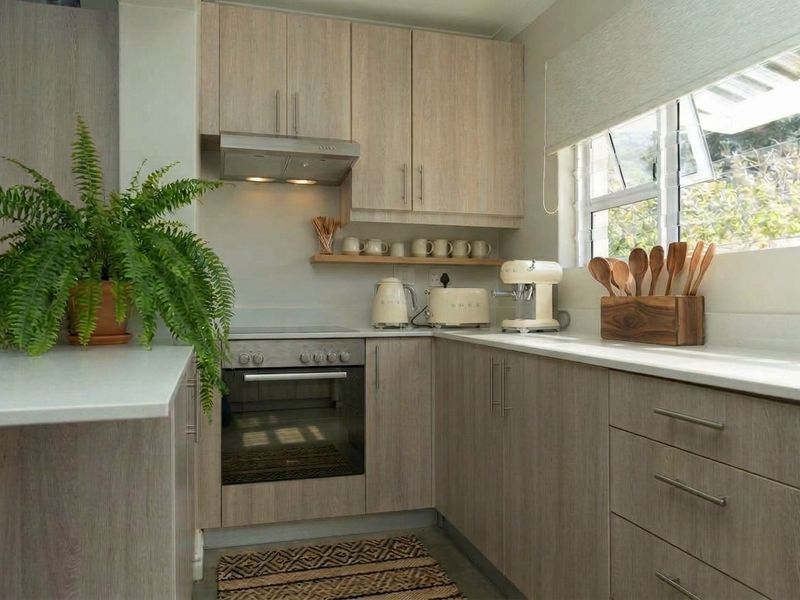 A modern, well-maintained kitchen featuring light wood-grain cabinetry, integrated oven and hob, extractor fan, and clean stone countertops with ample natural light.