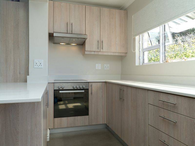 A clean, modern kitchen featuring light wood-grain cabinetry, stone countertops, a built-in oven, and an electric hob with an integrated extractor fan.