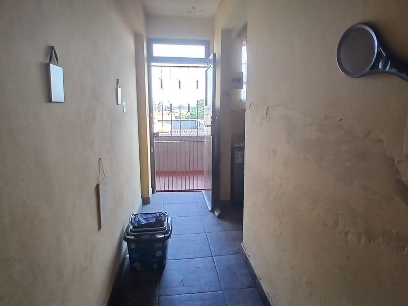 A narrow hallway featuring tiled flooring and a security gate leading to an outdoor area, showing significant signs of wall surface wear and peeling paint.