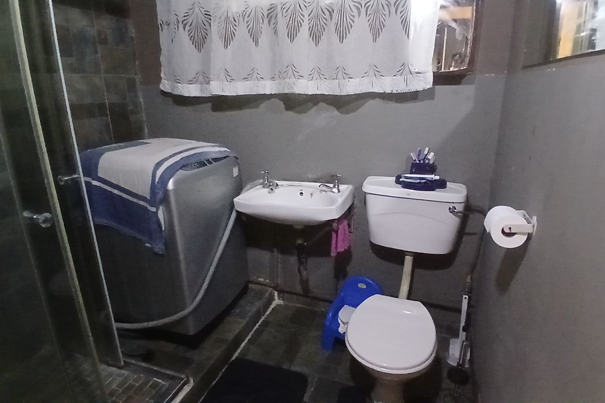A compact bathroom featuring a shower enclosure, wall-mounted basin, and toilet, with tiled flooring and wall finishes in need of cosmetic updates.