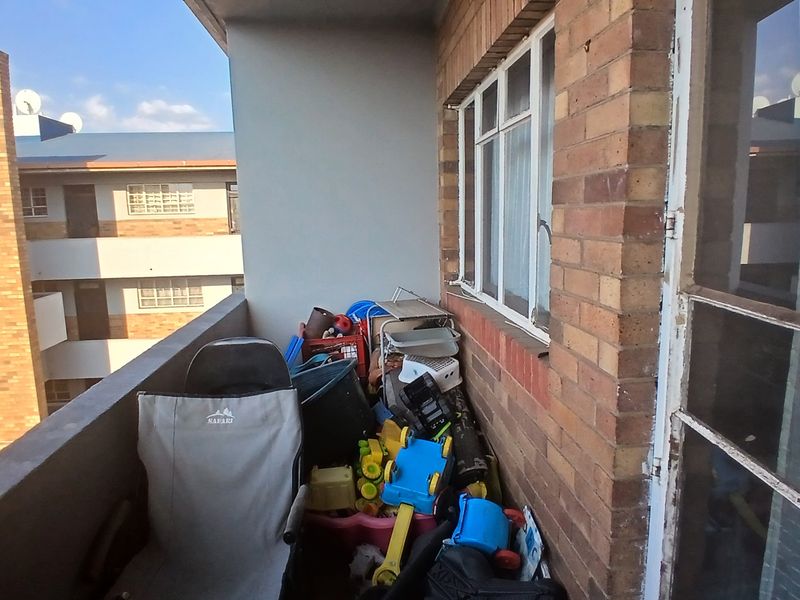 A compact balcony area featuring exposed brickwork and aluminum window frames, offering an outdoor space ready for revitalization.