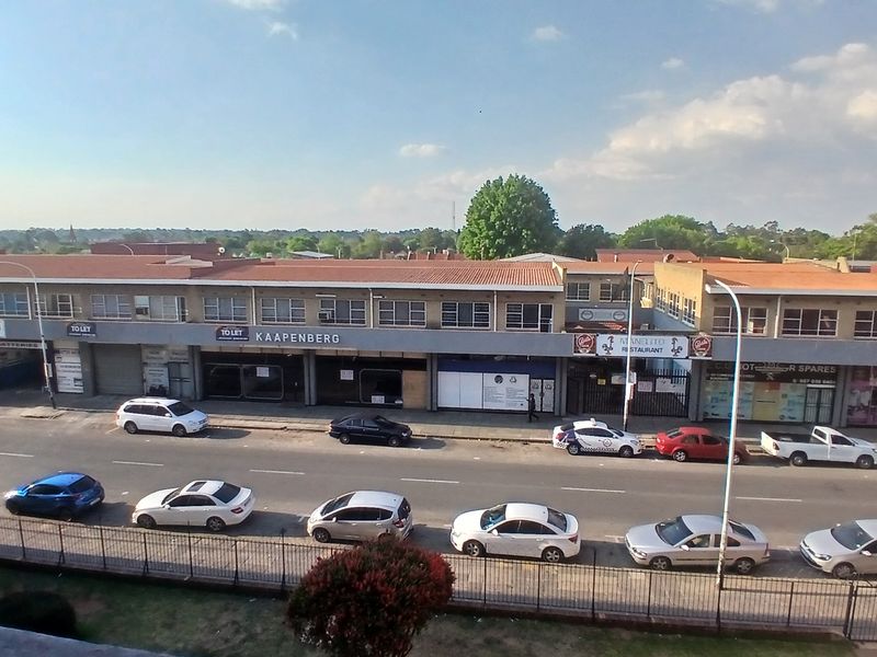 An elevated street view showing a commercial building complex with multiple storefronts, tiled roofing, and adjacent street parking.