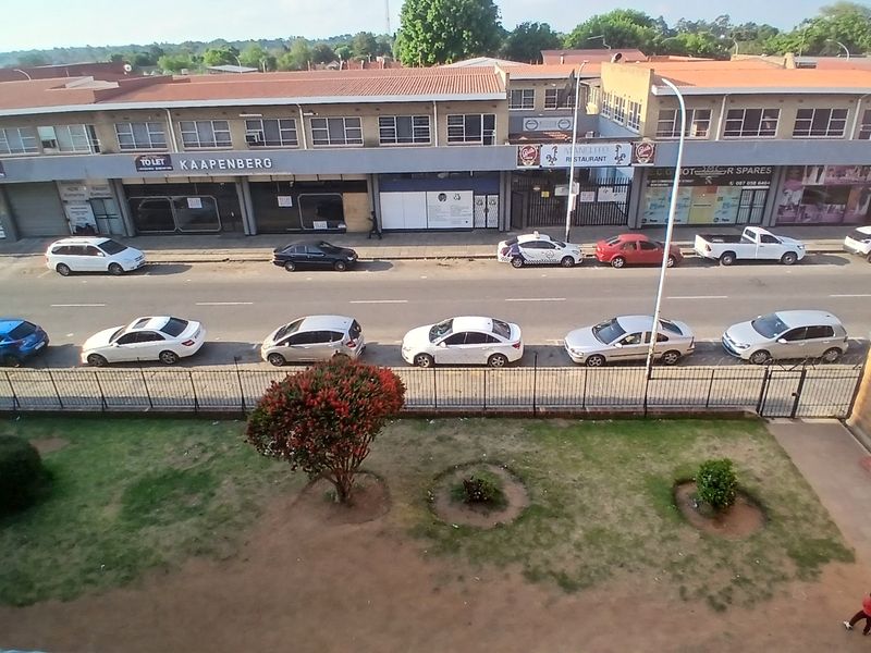 Elevated view overlooking a street with commercial storefronts, parking area, and a small garden space below.