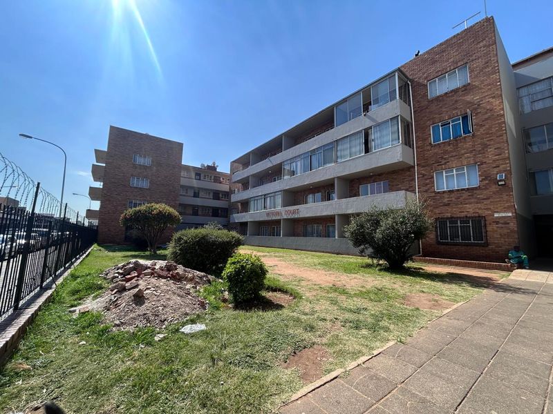 Exterior view of Victoria Court townhouse complex featuring brick facade, balconies, and surrounding communal garden area.