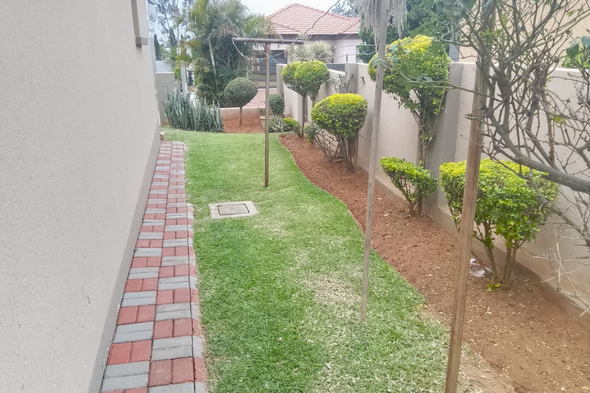 A side garden area featuring a paved walkway, manicured lawn, and boundary wall with established shrubbery.