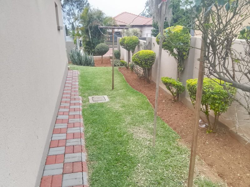 A side garden area featuring a paved walkway, manicured lawn, and boundary wall with established shrubbery.