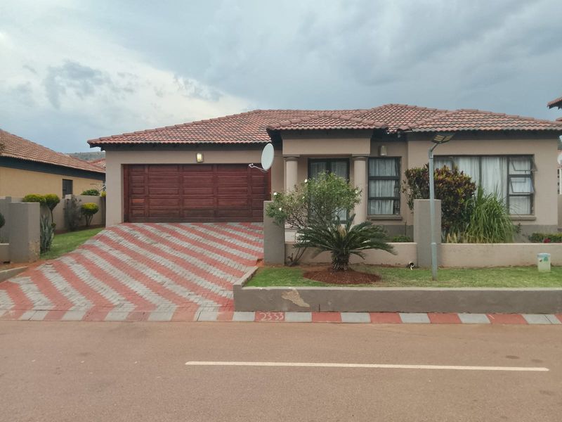 Front elevation of a single-story house featuring a tiled roof, double garage, and a paved driveway with a low boundary wall.