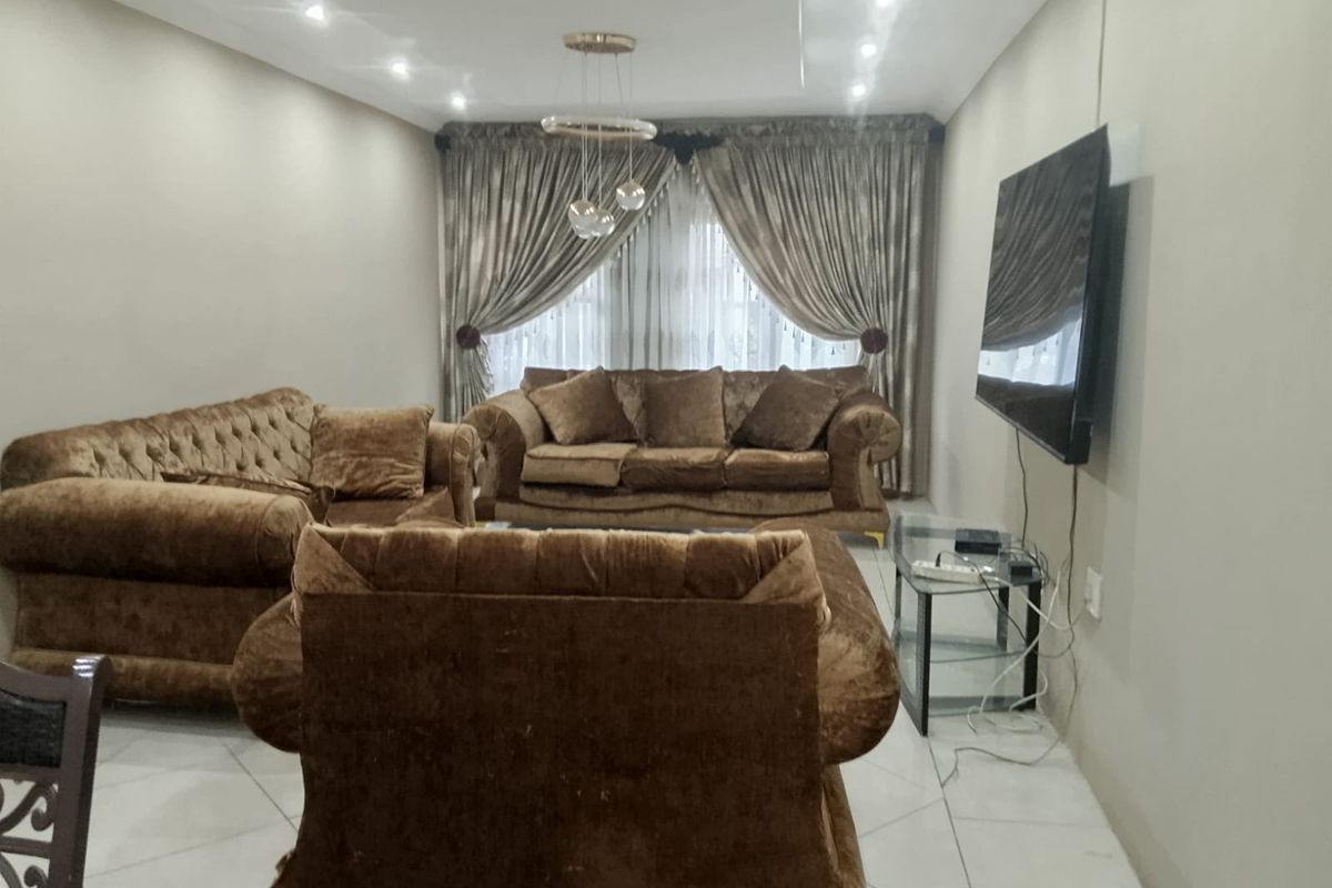 A spacious living room featuring neutral tiled flooring, recessed ceiling lighting, and a wall-mounted television setup.