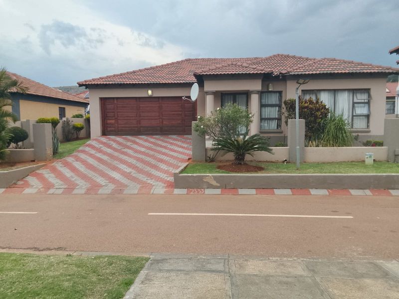 Front elevation of a single-story house featuring a tiled roof, double garage, paved driveway, and a low boundary wall with concrete pillars.