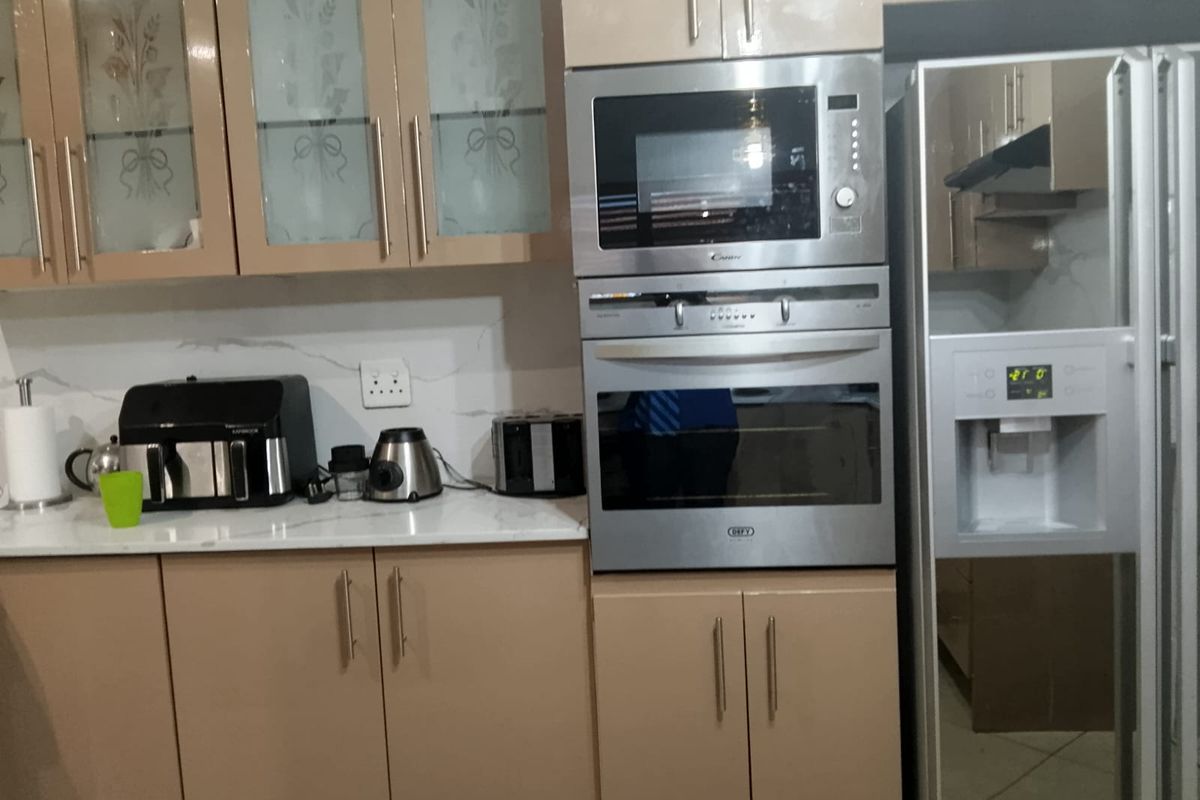 A modern kitchen featuring sleek beige cabinetry, marble-look backsplash, stone countertops, and integrated stainless steel appliances including an oven and microwave.