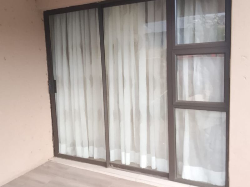 A covered patio area featuring tiled flooring and large sliding glass doors with aluminium frames, providing a clean and functional outdoor transition space.