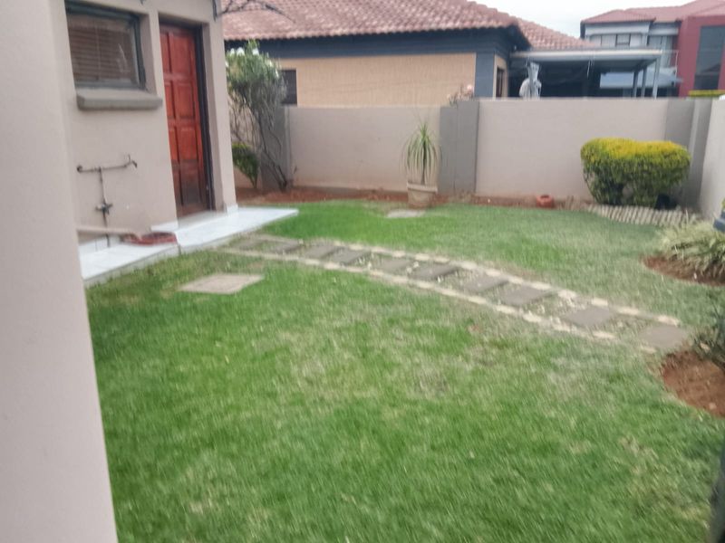 A private rear garden featuring a lawn, paved stepping stone pathway, and perimeter boundary wall, providing a functional outdoor space.