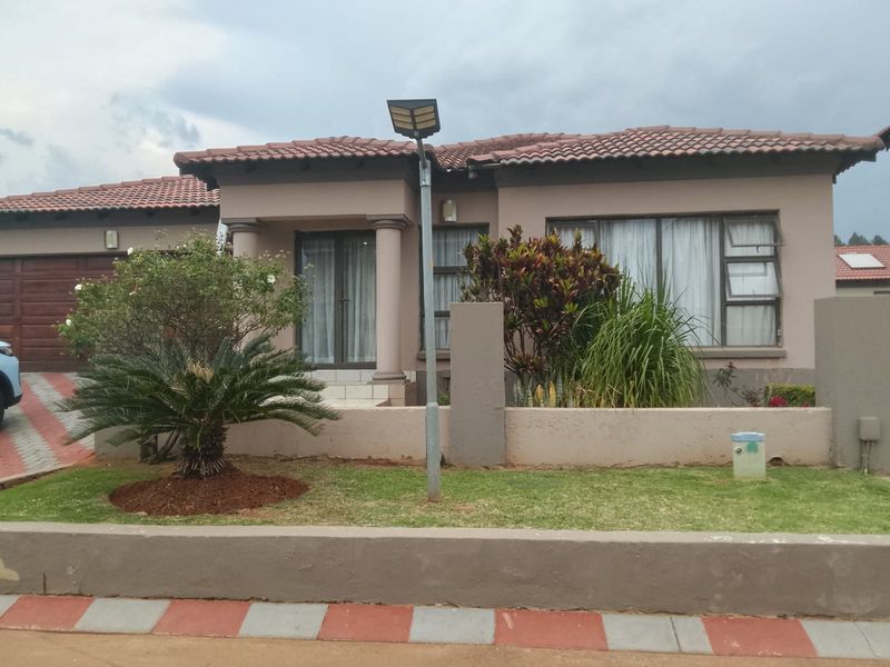 Front elevation of a single-story residential house featuring a tiled roof, paved driveway, integrated garage, and a landscaped front garden with boundary wall.