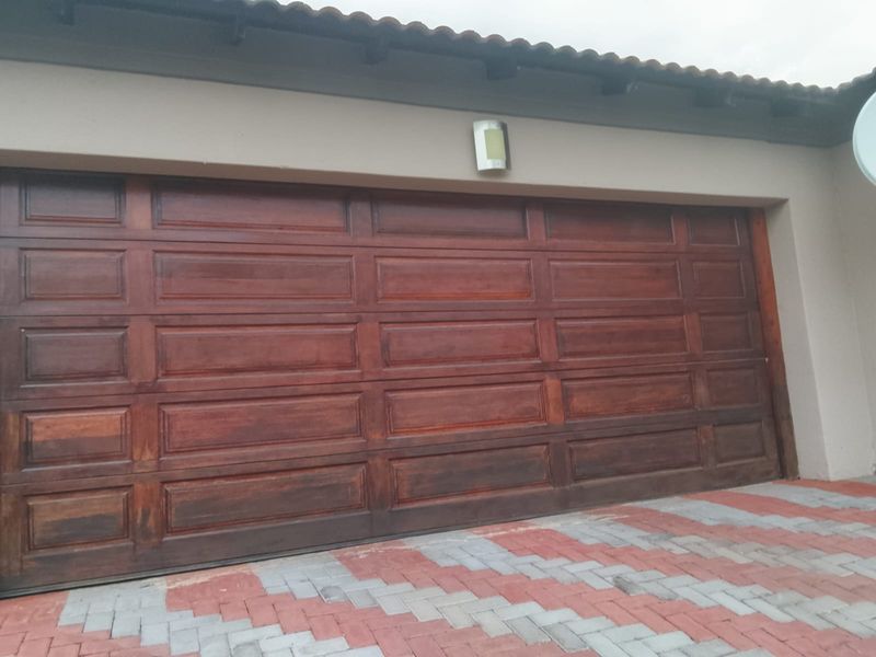 A double garage featuring a wooden sectional door, exterior wall lighting, and a paved driveway.