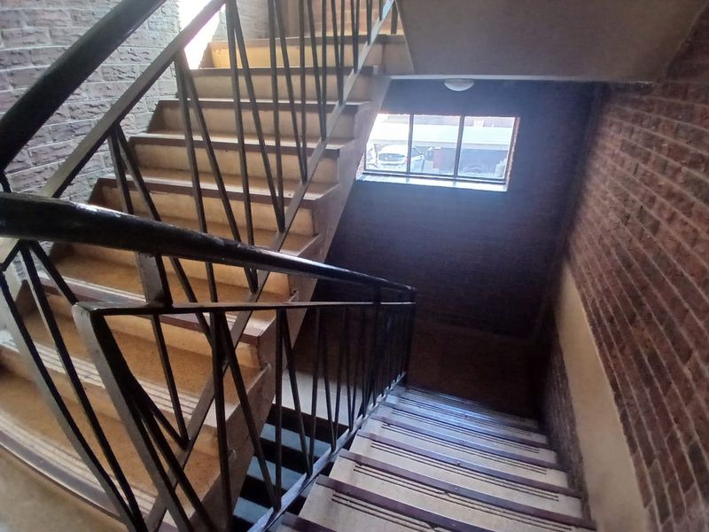 A functional stairwell featuring exposed brick walls, metal balustrades, and a window providing natural light to the landing area.