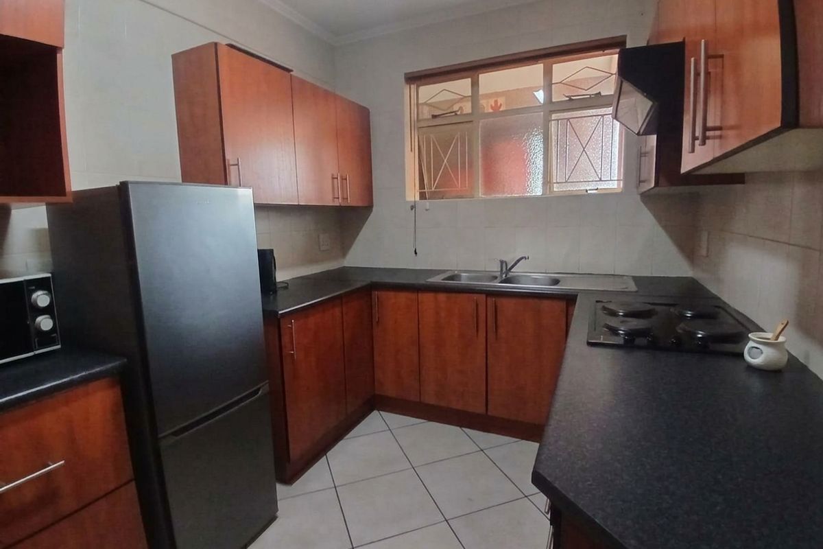 A functional kitchen featuring wood-finish cabinetry, dark countertops, a built-in hob with extractor fan, and tiled flooring.