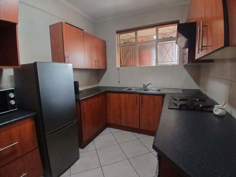 A functional kitchen featuring wood-finish cabinetry, dark countertops, a built-in hob with extractor fan, and tiled flooring.