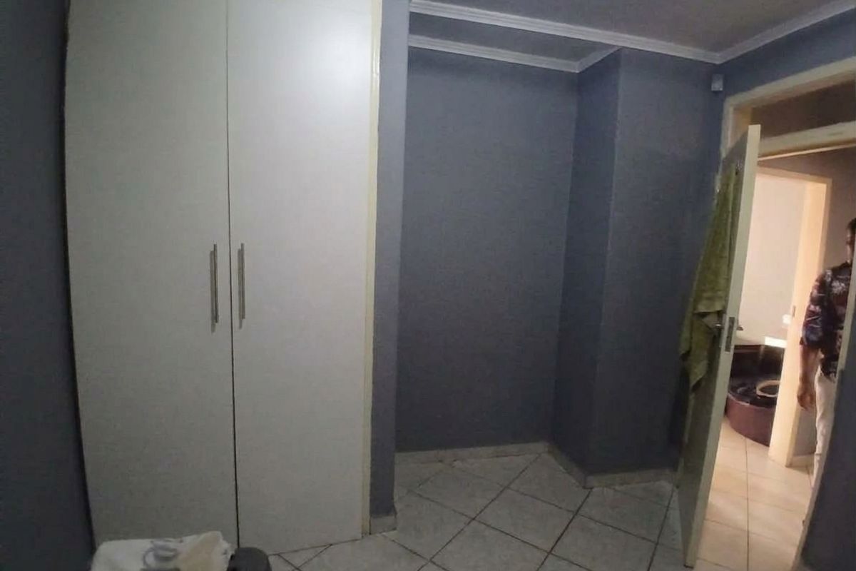 A bedroom featuring built-in wardrobes, tiled flooring, and neutral wall finishes, offering a blank canvas for potential interior updates.