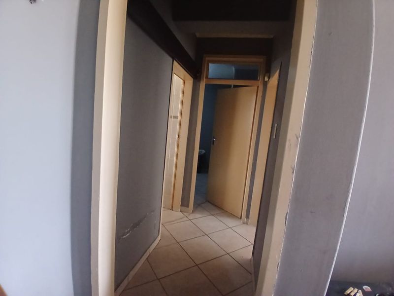 A narrow interior hallway featuring tiled flooring and multiple internal doorways, showing signs of wear on the walls and door frames.
