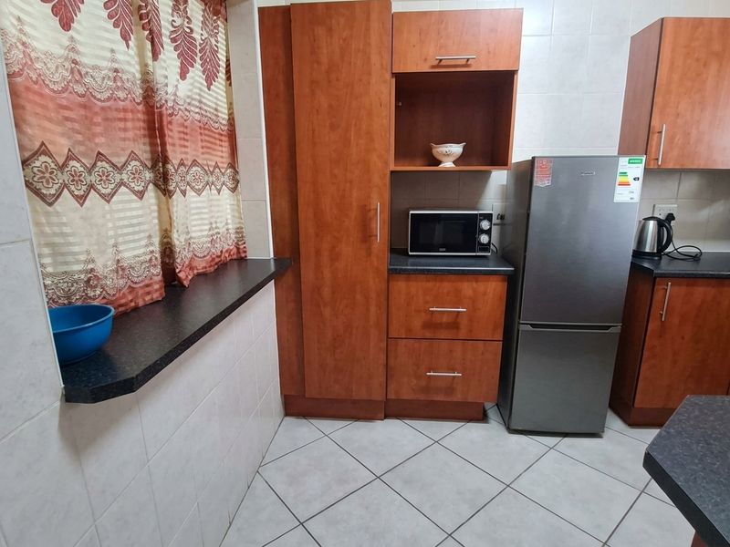 A functional kitchen featuring wood-finish cabinetry, dark laminate countertops, and tiled flooring with wall tiling throughout.