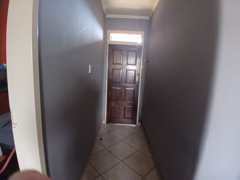 A narrow hallway featuring tiled flooring, a dark-toned panelled timber entrance door, and a transom window above the door frame.