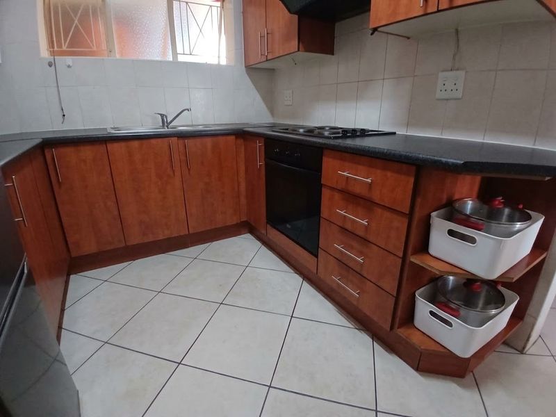 A functional kitchen featuring wood-look laminate cabinetry, dark countertops, a built-in oven with hob, and tiled flooring with a neutral backsplash.